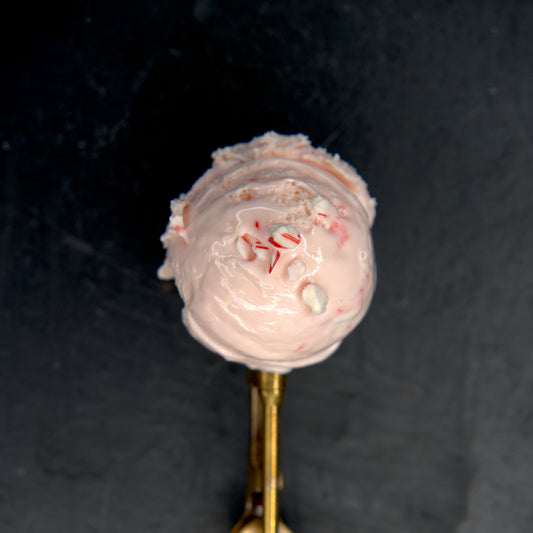 Pink ice cream with candy cane pieces on a gold spoon against a dark background