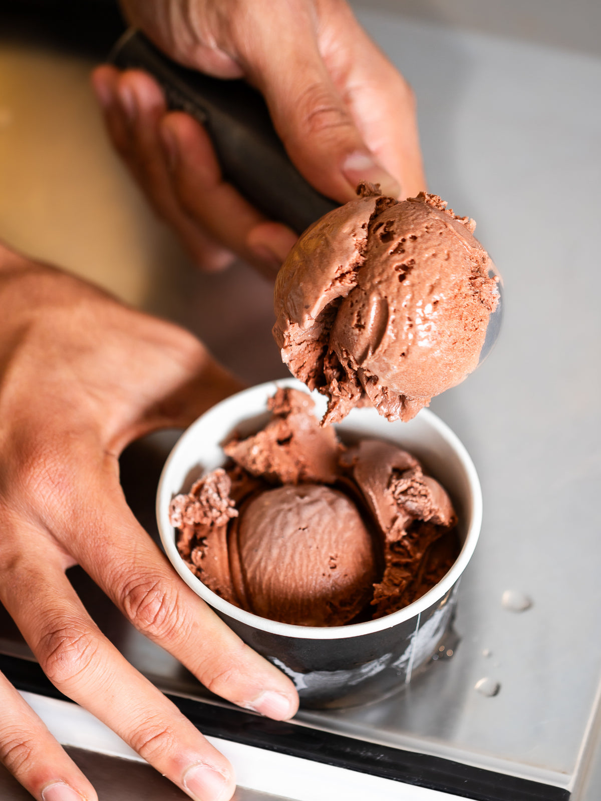 Chocolate ice cream being scooped into a bowl by hand