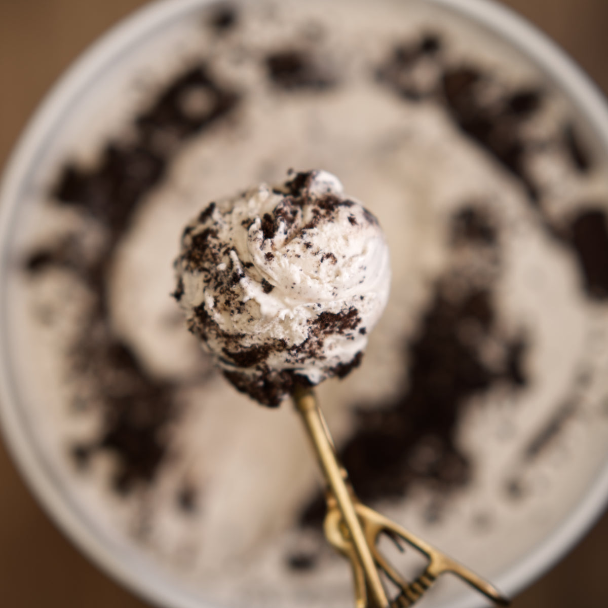 Ice cream scoop with Oreo cookie pieces on a spoon against a blurred dessert background