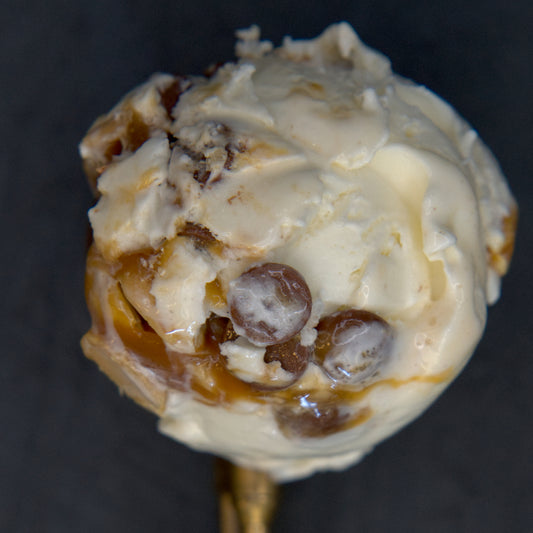Ice cream ball with chocolate chips and caramel on a gold spoon against a dark background