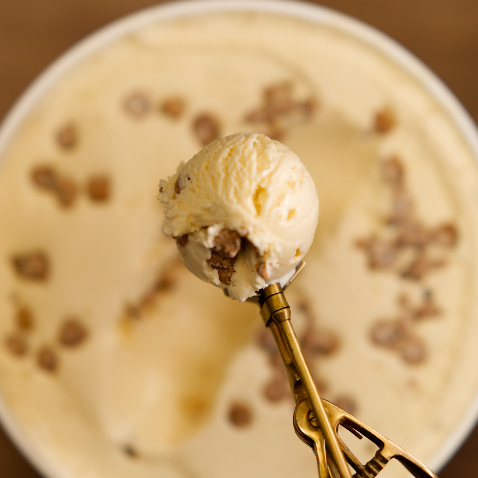 Gold spoon with a scoop of ice cream over a tub of ice cream